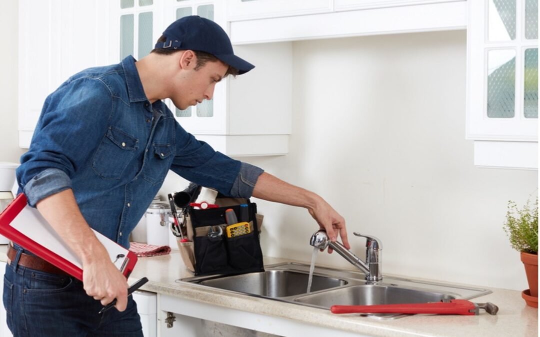 A plumber is fixing a faucet in a kitchen while holding a clipboard.