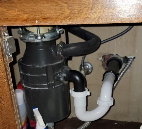 Black garbage disposal under a kitchen sink with a white PVC trap and the dishwasher hose connection
