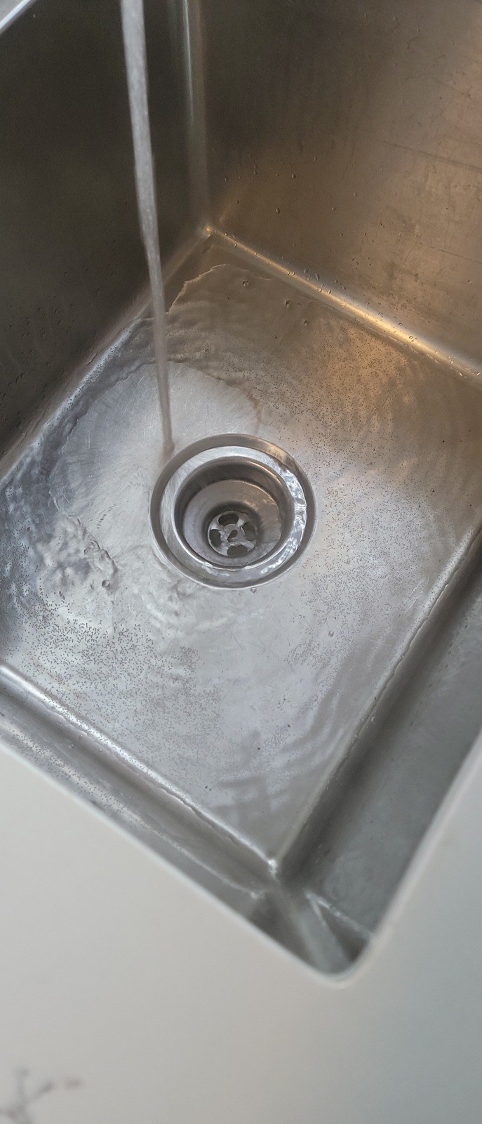 Water from the faucet running freely down the strainer of a stainless steel kitchen sink
