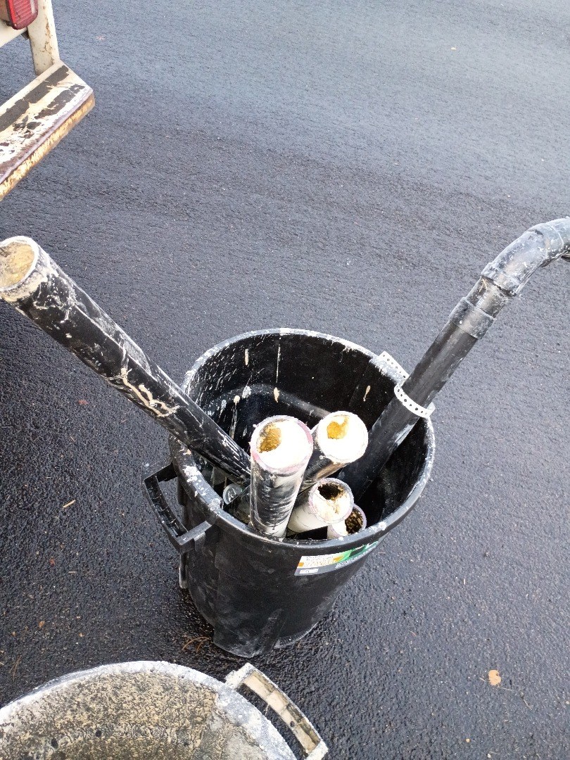 Cut lengths of old black ABS drain pipe standing in a trash can, their open ends packed solid with yellow grease