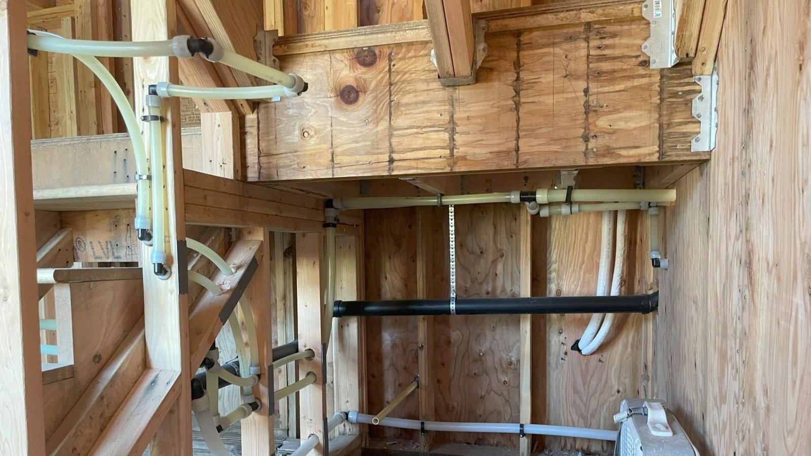 New PEX water lines and drain pipe run through open ceiling joists during a rough-in