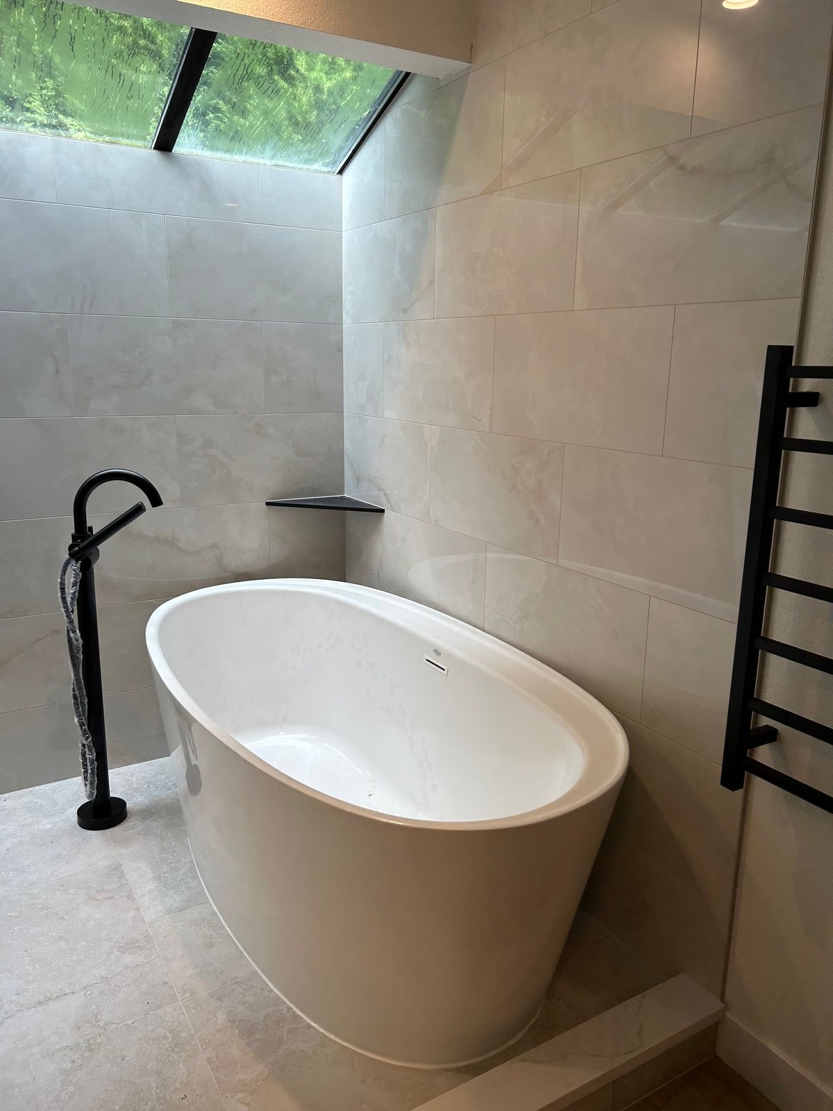 Freestanding oval bathtub with a matte black floor-mounted filler and a towel warmer on the wall