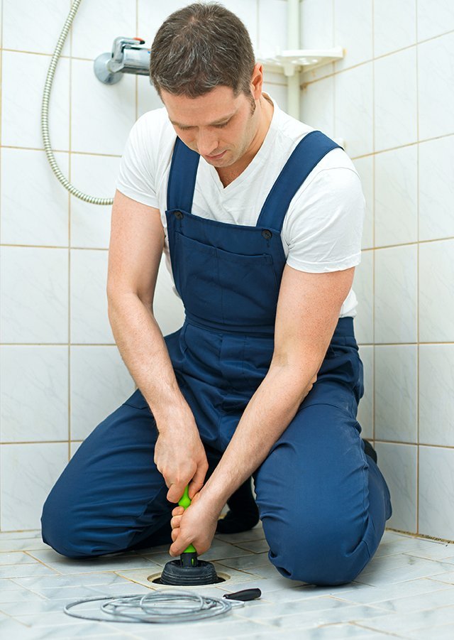 Plumber clearing a blocked drain with a hand auger under a sink