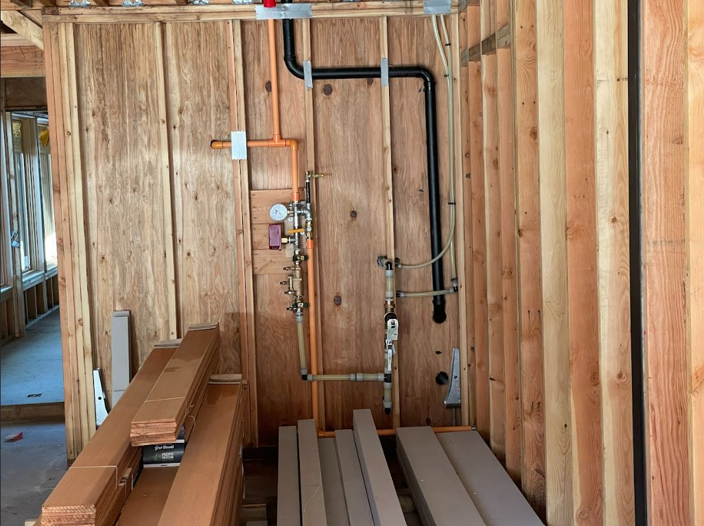 Copper and PEX supply lines with a pressure gauge and an ABS drain roughed in on a framed wall
