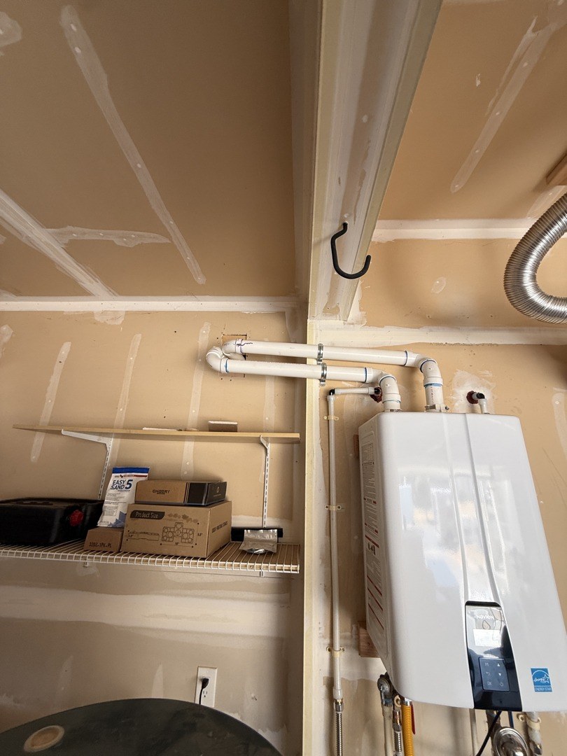 Two white PVC vent pipes running from the top of a wall-hung tankless water heater across a garage wall to the outside