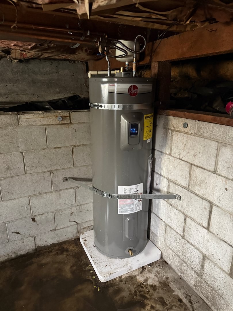 Gray 50-gallon electric water heater on a drain pan against a concrete-block wall, held by two seismic straps, with new flex connectors on top